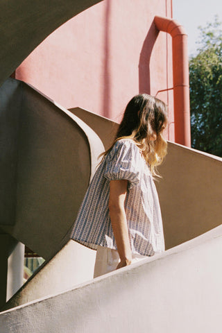 Woman in a dress standing on a modern architectural structure with a pink wall in the background