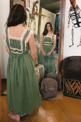 Woman in a green dress standing in front of a mirror in an interior setting.