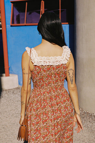 Woman wearing a floral dress with lace neckline, walking away from a colorful building.