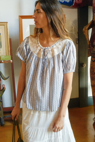 Woman wearing a patterned blouse and white skirt in an indoor setting