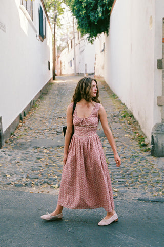 Woman in a pink dress walking down a narrow street with white walls.