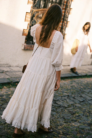 Woman in a white dress walking on a cobblestone street.