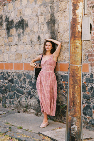 Woman in a pink dress leaning against a textured wall.