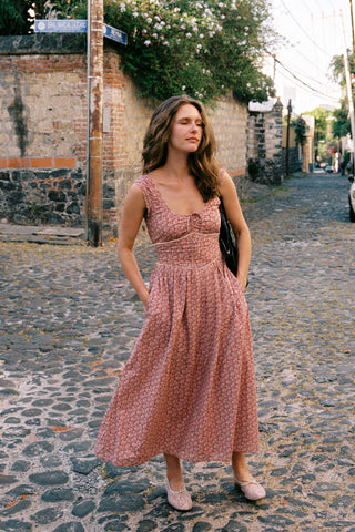 Woman in a pink dress standing on a cobblestone street.