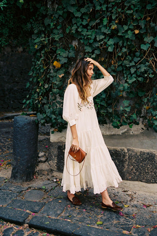 Woman in a white dress standing against a green ivy wall.