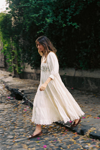 Woman in a white dress walking on a stone path with greenery in the background