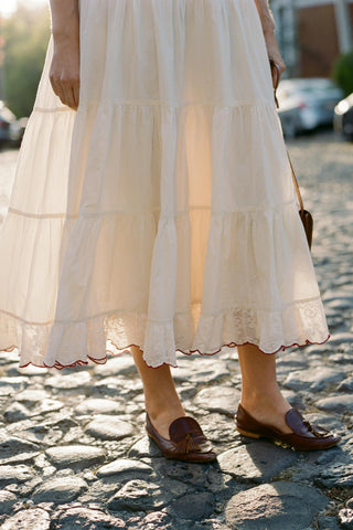 Person wearing a white dress with ruffled layers on a cobblestone street.