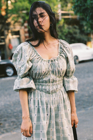 Woman wearing a light green floral and plaid dress with puffed sleeves on a street.