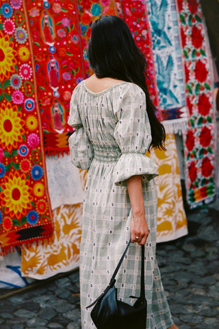 Woman in a green floral and plaid dress  standing in front of colorful fabric displays.