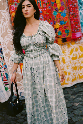 Woman in a green floral and plaid dress standing in front of colorful fabric