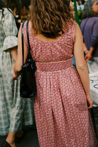 Woman in a pink floral dress walking through a crowd.