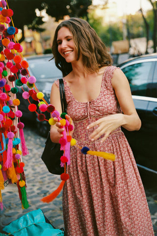 Woman in a pink dress standing next to colorful pom-pom decorations on a street.
