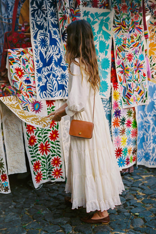 Woman in a white dress standing in front of colorful embroidered textiles.