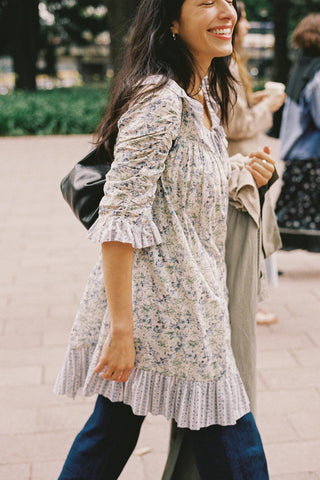 Woman in a floral dress walking outdoors on a sidewalk.