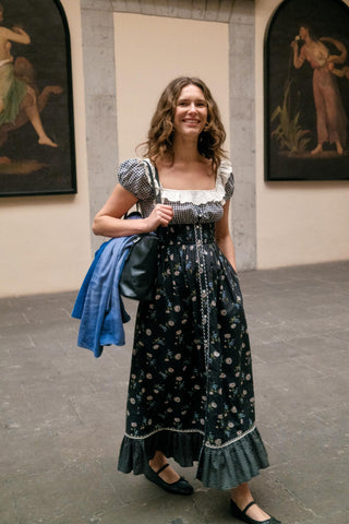 Woman in a floral dress standing in an art gallery with paintings on the wall.