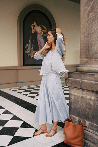 Woman in a light blue outfit standing in an elegant interior setting with a checkered floor.