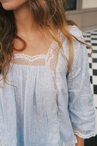 Light blue blouse with lace details worn by a person, with a checkered floor in the background.