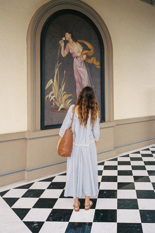 Woman in a light blue outfit standing in front of a wall painting with a checkered floor.