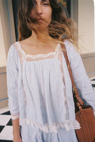 Woman wearing a light blue blouse with lace details, holding a brown leather bag.