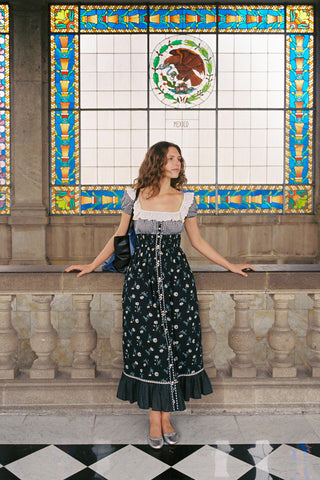 Woman in a floral dress standing in front of a decorative stained glass window.