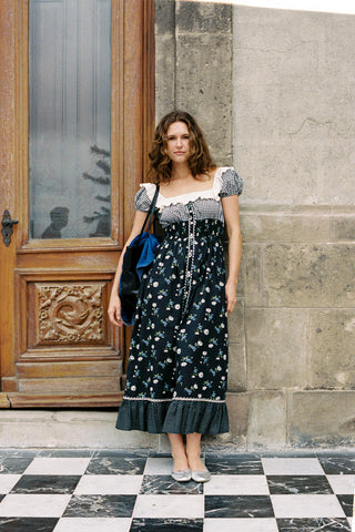 Woman in a floral dress standing in front of a stone wall and wooden door.