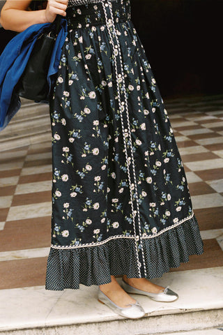 Person wearing a black floral skirt with white trim on a checkered floor.