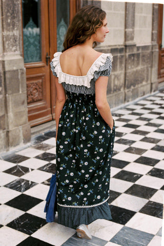 Woman in a floral dress standing on a checkered floor with stone walls in the background