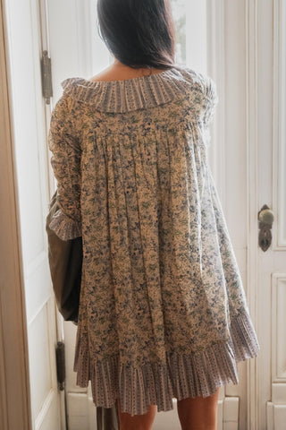 Person wearing a floral patterned dress standing in front of a white door.