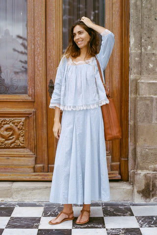 Woman in light blue outfit standing in front of a wooden door.