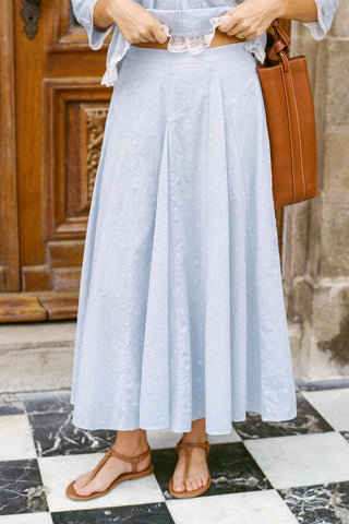 Person wearing a light blue skirt with a brown handbag in front of a wooden door.