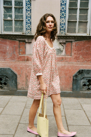Woman in a floral dress holding a yellow bag in front of a building with decorative tiles.