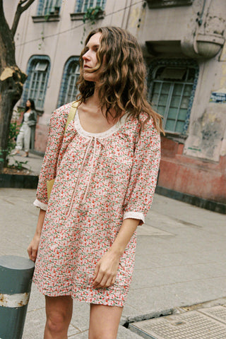 Woman in a floral dress standing on a street with buildings in the background