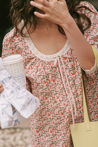 Person wearing a floral dress holding a coffee cup and a newspaper.