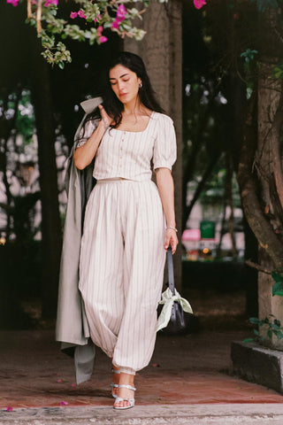 Woman in a light-colored outfit walking outdoors with greenery in the background