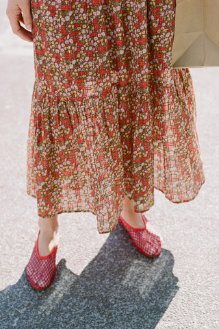 Person wearing a red floral dress and red shoes on a textured surface