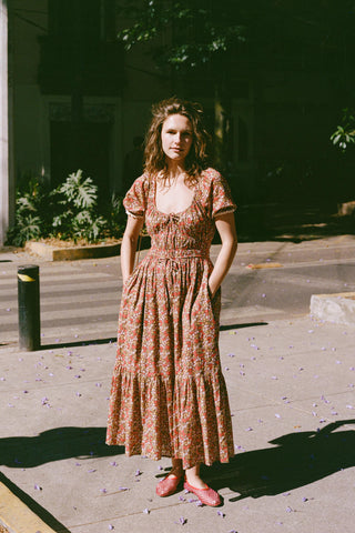 Woman in a red floral dress standing outdoors on a sunny day