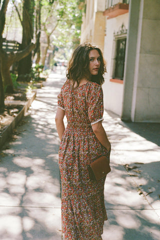 Woman in a dress floral dress walking down a street on a sunlit day.