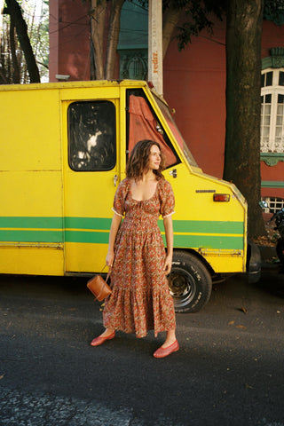 Woman in a red floral dress standing next to a yellow van with green stripes.