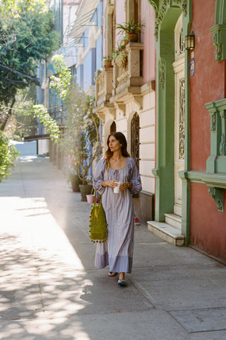 Woman in a striped dress walking down a sunlit street with colorful buildings.
