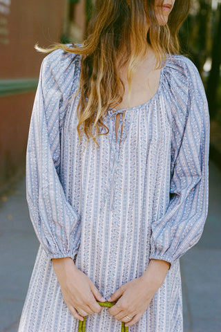 Woman wearing a blue patterned dress with long sleeves in an outdoor setting