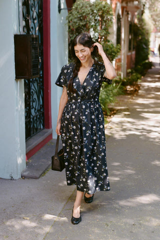 Woman in a black floral dress walking down a sidewalk.