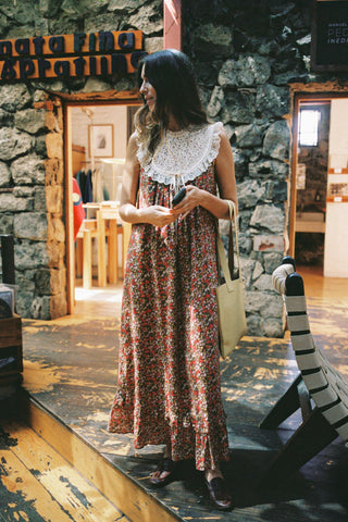 Woman in a floral dress standing in a stone-walled room with wooden floors.