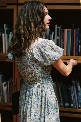 Woman in a floral dress standing in front of a bookshelf