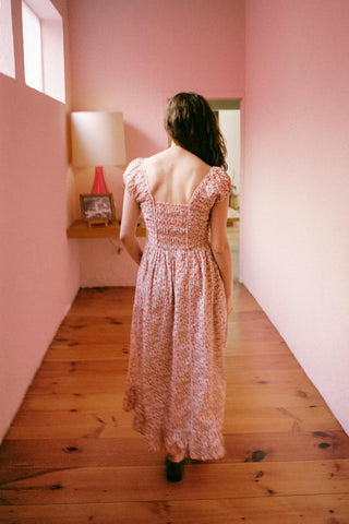 Woman in a pink dress standing in a room with pink walls and wooden floor.