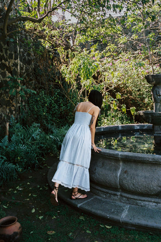 Woman in a light blue dress standing by a fountain in a garden setting