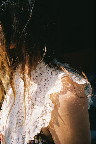 Person wearing a white lace bib with sunlight casting shadows on their skin.