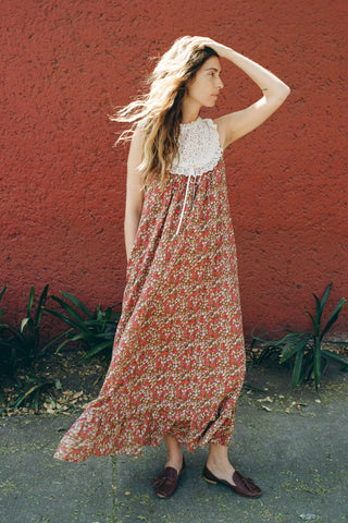 Woman in a floral dress standing against a red wall.