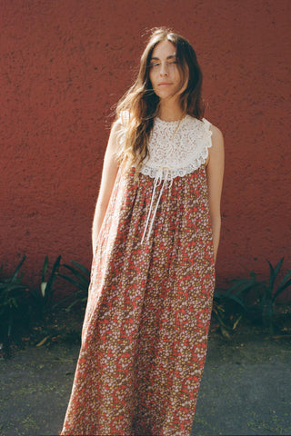 Woman wearing a floral dress with a white lace bib against a red wall.