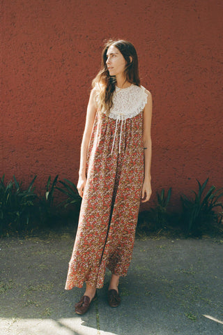 Woman in a floral dress standing against a red wall with greenery.
