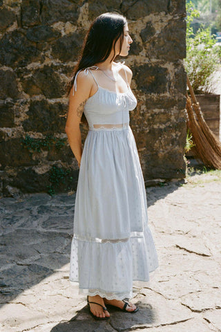 Woman in a light blue dress standing against a stone wall.